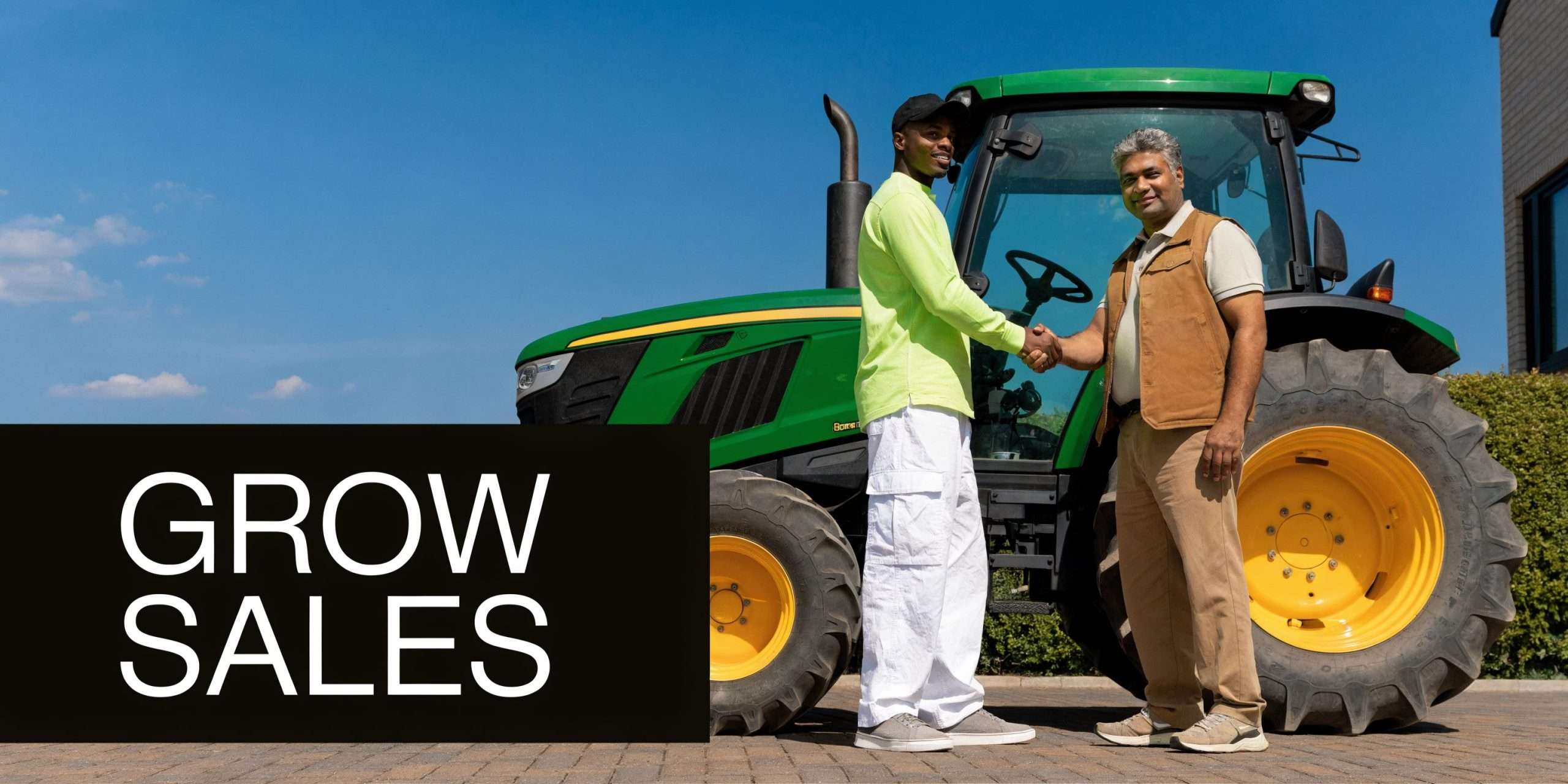 A young man and an older man shaking hands in front of a large green farm tractor.